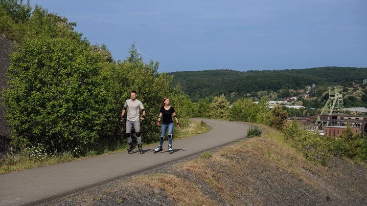 Ein Mann und eine Frau fahren Inliner auf einem asphaltierten Weg von dem man einen weiten Blick hat.
